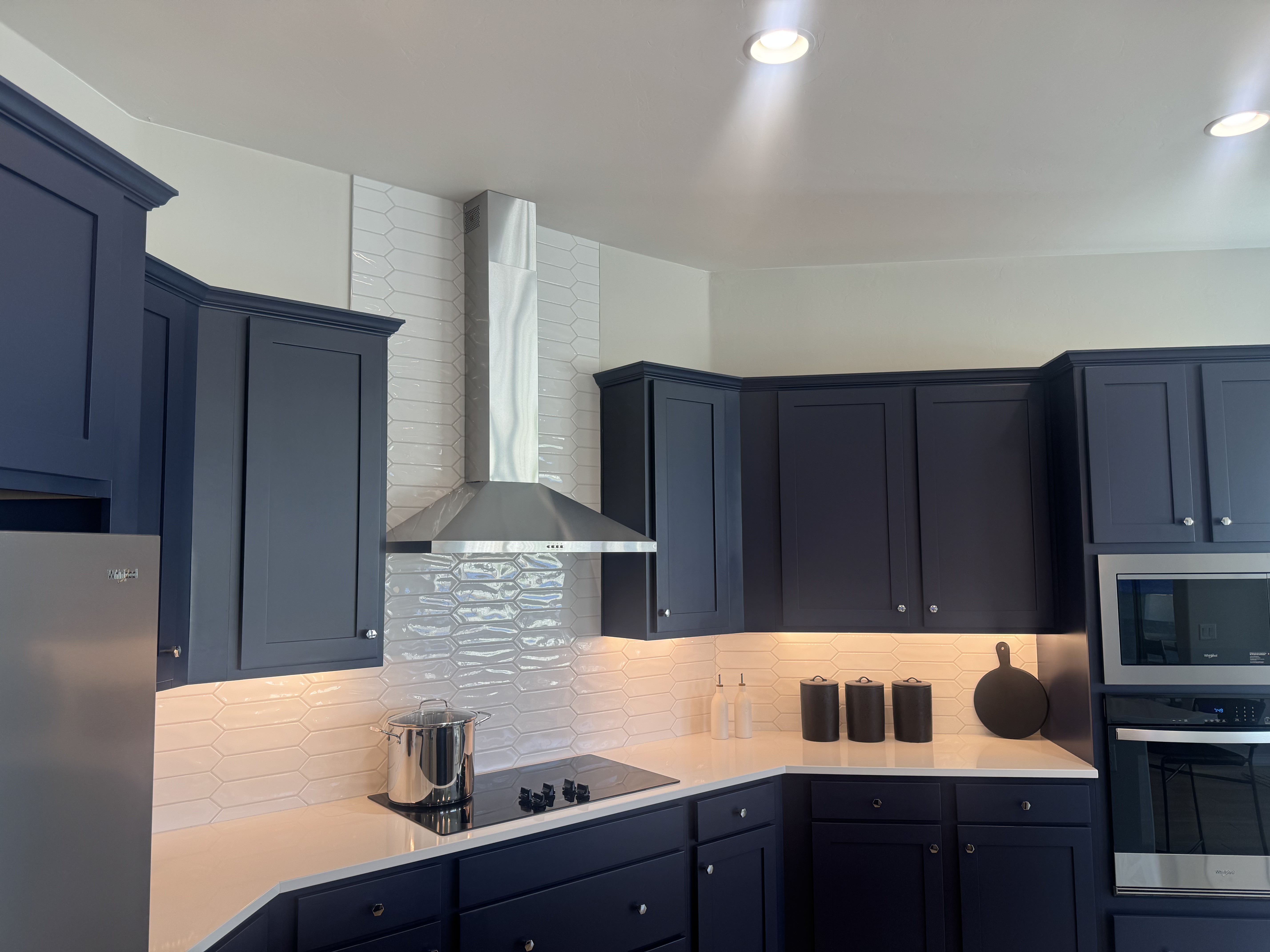 White shaker cabinets with light countertops, gray subway backsplash, and farmhouse sink under windows